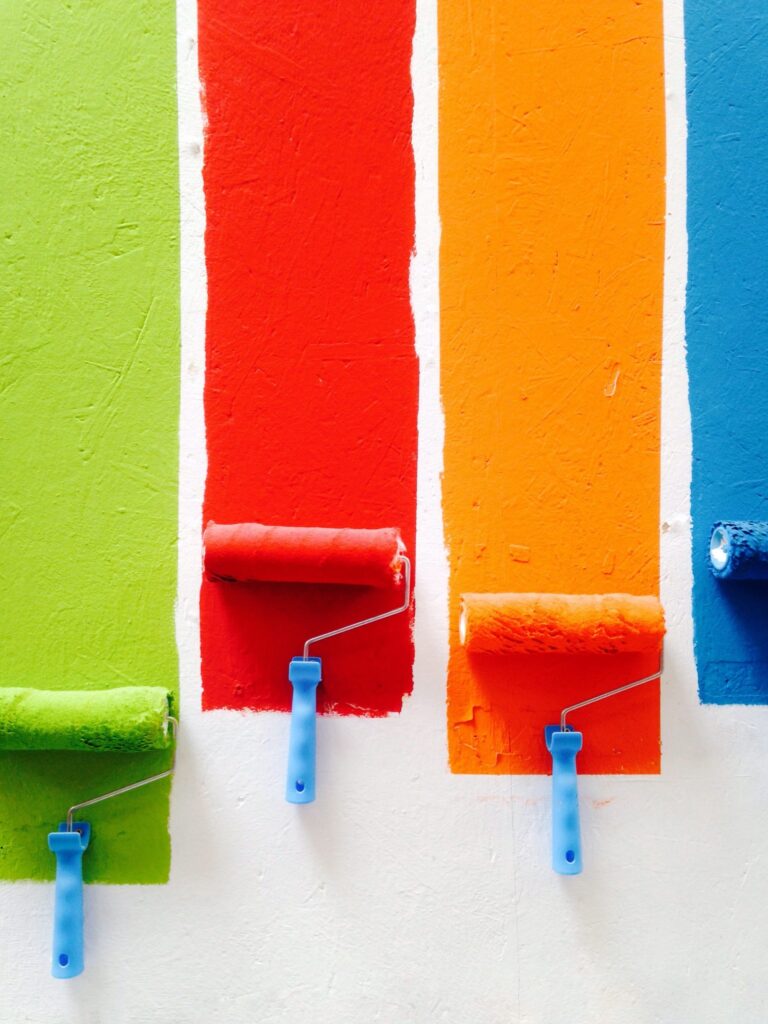 Green, red and orange paint being rolled on a wall